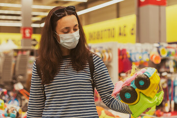 Woman in a protective mask in a supermarket chooses children's toys. Woman in medical mask at the supermarket toned