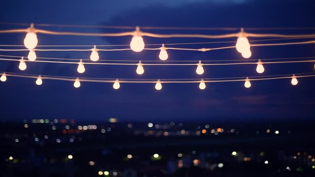 garland outdoor lights swaying in the wind at night with city lights on the background