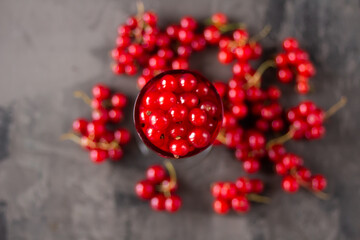 Red currant in a shot glass, the rest is scattered around it on a gray textured background