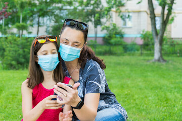 Mom with daughter in the park in medical masks. Family of mom and kid wearing protective medical...