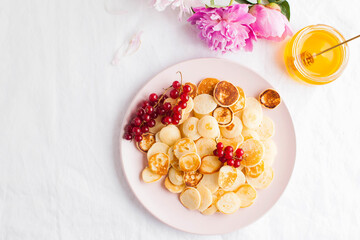 Tiny pancakes with berries, honey, flowers. Pancake cereal. The concept of Breakfast, food trends. Copy space.