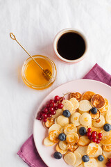 Tiny pancakes with berries, honey, coffee. Pancake cereal. The concept of Breakfast, food trends. Copy space.