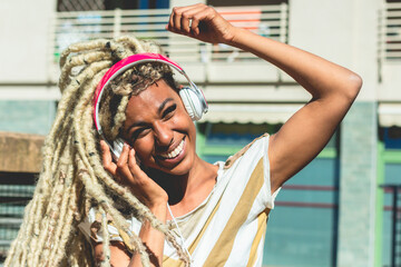 African girl moving blond dreadlocks hair wearing while listening music playlist with headphones -...