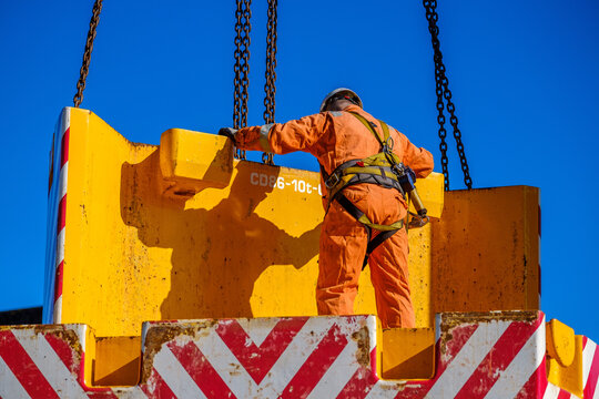 Worker in orange suite and hard hat positions heavy counterweight on mobile crane