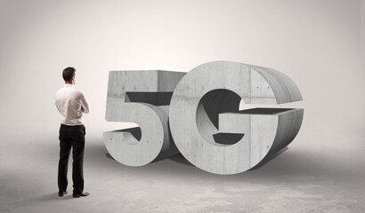 Rear view of a businessman standing in front of 5G abbreviation, modern technology concept