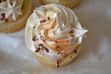 Tasty cupcake with white and gold cream, with chocolate topping, on a milk background.