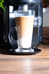 A studio shot of three-layered cup of coffee being poured by a coffee machine