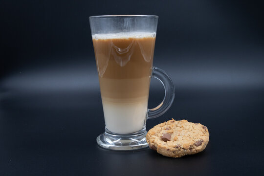 A studio shot of three-layered coffee drink and chocolate chip cookies in black grey background