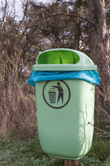 grüner Mülleimer mit blauem Müllsack und Piktogramm in einem Park im Winter