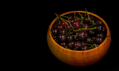 Cherry in a wooden bowl on a black background