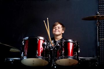 The child sits with drumsticks in his hands. Studying in the studio.