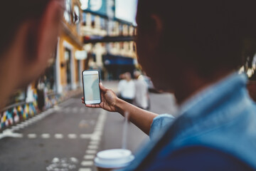 Cropped back view of man and woman holding smartphone device your elongated hand and using internet navigator on blurred background of urban setting.Modern mobile phone with travel app