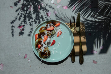 tofu curd pancakes with matcha and slices strawberries on a blue plate, shadow of a palm branch, side view