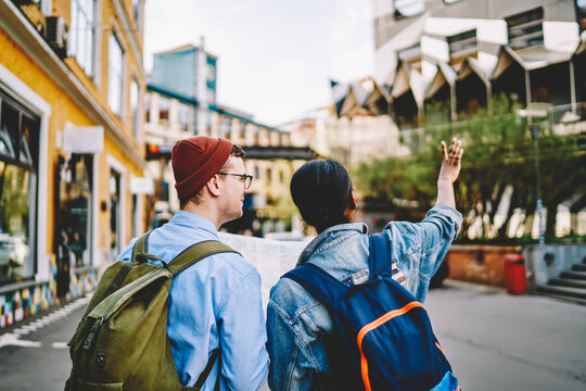Back view of multicultural tourists dressed in casual wear walking on streets in urban street of new city during weekend's trip.Couple in love strolling and enjoying showplaces during travel tour