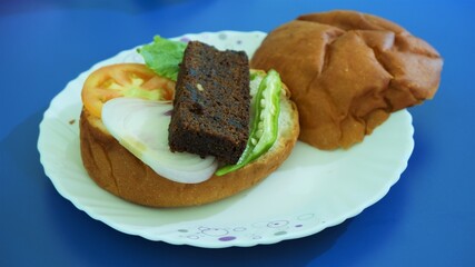 stuffed big burger on white plate and blue background