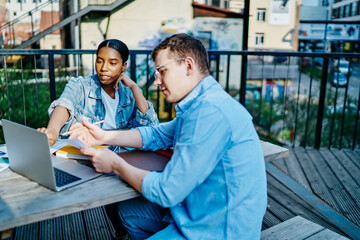 Professional male and female multiracial colleagues discussing cooperation on online business using laptop computer for job, young  woman and man watching video on netbook discuss information