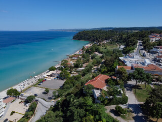 Fototapeta na wymiar Chalkidiki, Greece coastal village landscape drone shot with pine trees. Aerial day view of Kallithea seafront at Kassandra peninsula with a beach bar by a clean tranquil blue sea.