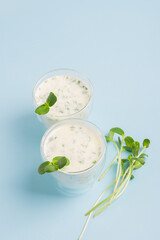 Dairy product drink with the addition micro grass sprouts in glasses on a blue background. Vertical frame copy space