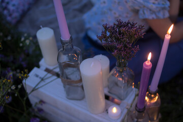 
White candles, violet candles and violet flowers in transparent glass bottles stand on a wooden...