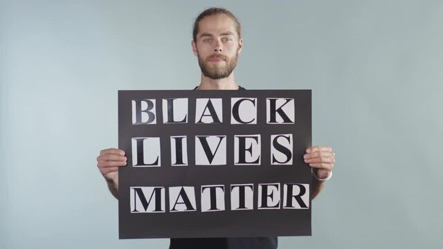 Handsome young man hold poster Black Lives Matter on grey background racial morality society peace human text words can kill torture close up slow motion