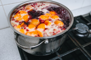 Cooking a delicious compote of apricot, apples, cherries, raspberries. Fresh fruits are boiled in boiling water in a metal pan on the stove. Photography, concept.