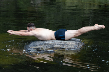 A swimmer guy lies horizontally on a stone among the water of a river and forest