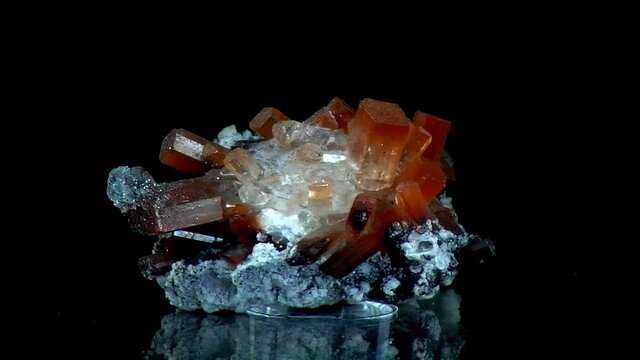 Close up of a turning rock matrix with clear and orange crystals of topaz and black background