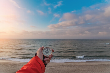 First-person view of a female hand with a compass on a background of a beautiful sea landscape. The...