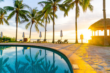 Umbrella and chair around swimming pool in hotel resort with sunrise in morning