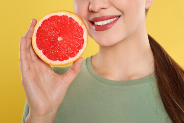 Young woman with cut grapefruit on yellow background, closeup. Vitamin rich food