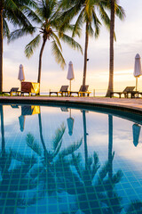Umbrella and chair around swimming pool in hotel resort with sunrise in morning