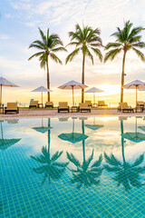 Umbrella and chair around swimming pool in hotel resort with sunrise in morning