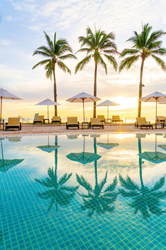 Umbrella and chair around swimming pool in hotel resort with sunrise in morning