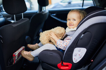 Adorable toddler girl in modern car seat with her favorite stuffed toy