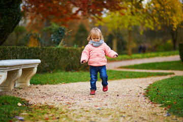 Adorable cheerful toddler girl running in Montsouris park in Paris