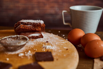 Chocolate cakes stacked on a wooden table. next to it are eggs and pieces of chocolate. blurred background