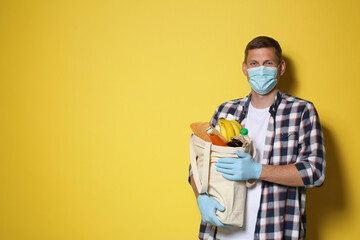 Male volunteer in protective mask and gloves with products on yellow background, space for text....