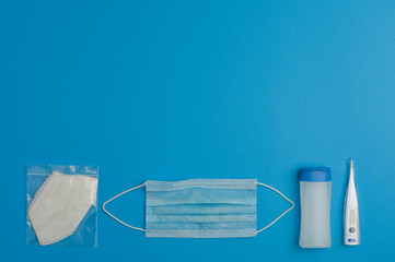 prevention concept covid-19, gel with blue cap, digital thermometer, blue mask, white mask in protective bag, white tissue paper in protective bag, blue background, write space
