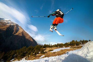 man skier in flight after jumping from a kicker in the spring against the backdrop of mountains and...