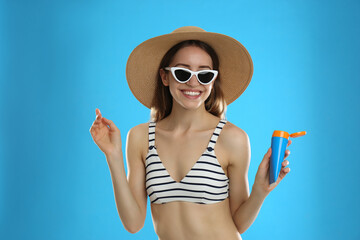 Young woman with sun protection cream on light blue background