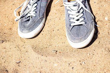 grey sneakers with white laces on a sandy beach - Powered by Adobe
