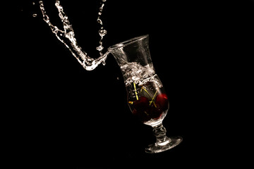 Red cherry dropped into the glass of water with splash on black background