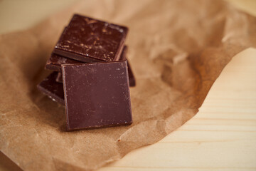Pieces of chocolate bar lie on crafted brown paper. Close-up.With copy space.