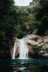 Naklejka premium Vertical photo of a high mountain river waterfall between trees and vegetation