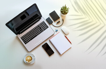 Desk with laptop, work accessories and coffee with copy space, shadow of a plant