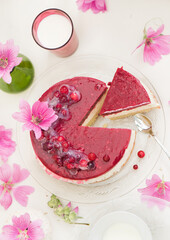A food photograph of a coconut pie with vanilla mousse covered with a cranberry gelled layer. The decor used pink fresh flowers.