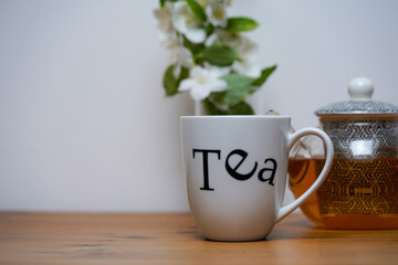 Cup of jasmine tea, tea pot and white jasmine flowers in the vase, white and wooden background