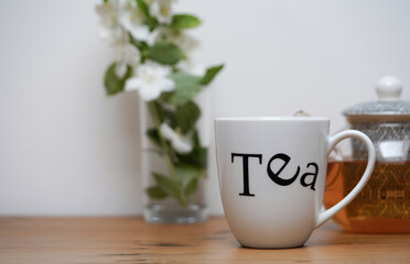 Cup of jasmine tea, tea pot and white jasmine flowers in the background., on wooden table 