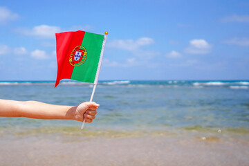 Hands of kid girl holding Portugal flag against the sea horizon. Independence Day concept.