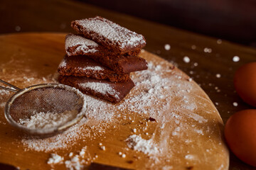 Chocolate cakes stacked on a wooden table. next to it are eggs and pieces of chocolate. blurred background